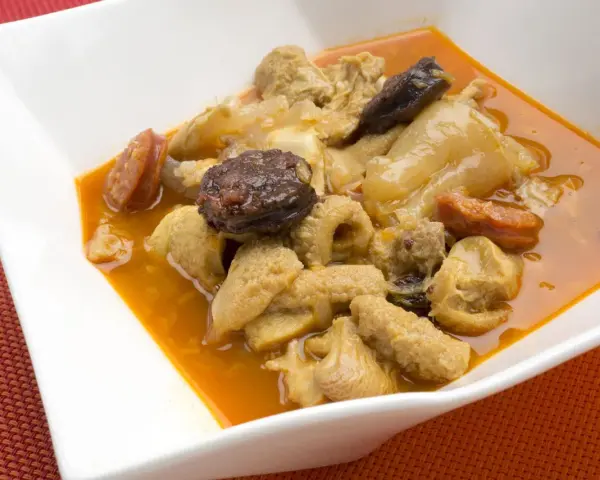 Un plato de callos a la madrileña con chorizo y morcilla en una cazuela blanca.