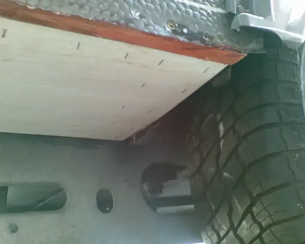 Naprawa podłogi w przyczepie kempingowej: nowa sklejka mocowana do ramy, obok koła.