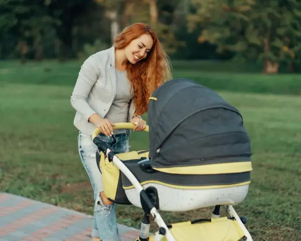 Uśmiechnięta mama z rudymi włosami pochyla się nad wózkiem. Idealny spacer, gdy zastanawiasz się, jak ubrać niemowlę 20 stopni.