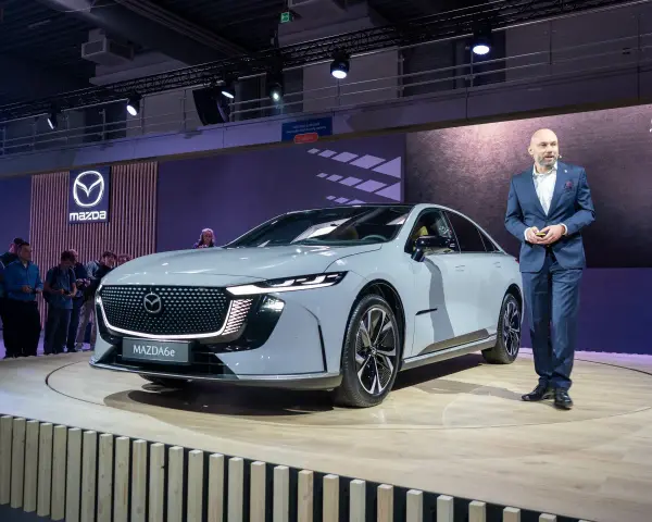 Elegancki, szary sedan Mazda6e prezentowany na scenie przez mężczyznę w garniturze.