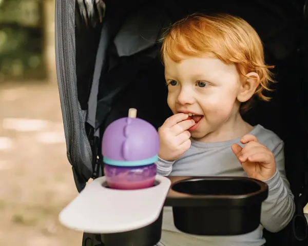 Rotschopf-Kind im Kinderwagen, isst genüsslich einen Snack. Dieses Kind hat immer Hunger und freut sich über jede Leckerei.