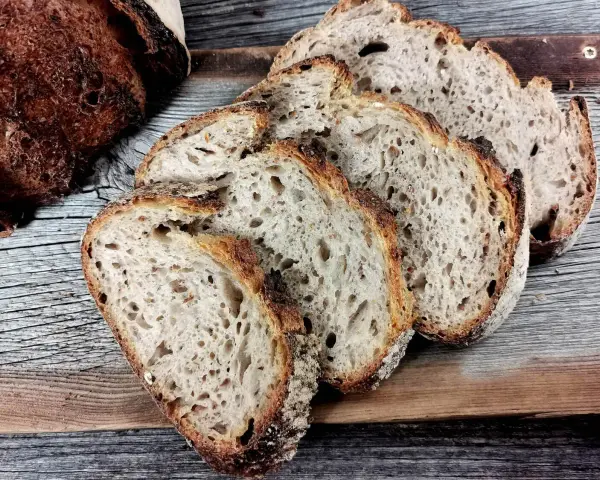 Ein Laib Sauerteigbrot, angeschnitten, mit sichtbarer, knuspriger Kruste. Die Scheiben zeigen eine luftige Krume. Hoffentlich ist die brotkruste zu hart, um sie zu genießen.