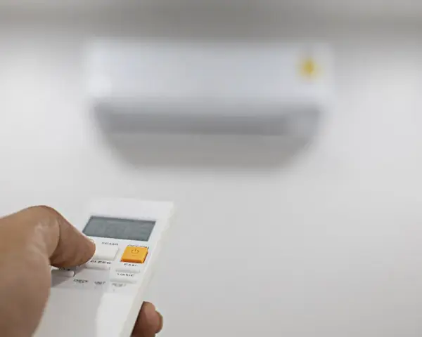 Mano che preme il telecomando per regolare il condizionatore. Il suo significato è comfort e controllo della temperatura.