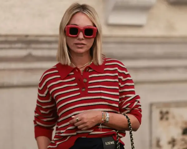 Donna con occhiali rossi oversize e maglione a righe rosse e bianche, un look che evoca un sofisticato preppy style.
