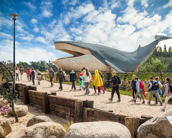Grupa dzieci zwiedza park z gigantycznym modelem wieloryba. Władysławowo atrakcje dla dzieci oferują niezapomniane wrażenia.