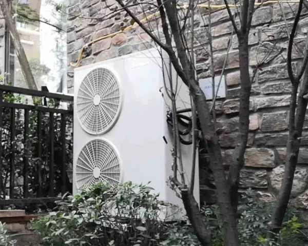 Dwa wentylatory jednostki zewnętrznej klimatyzatora sprsun, zamontowane na kamiennej ścianie, otoczone zielenią i gałęziami drzew.