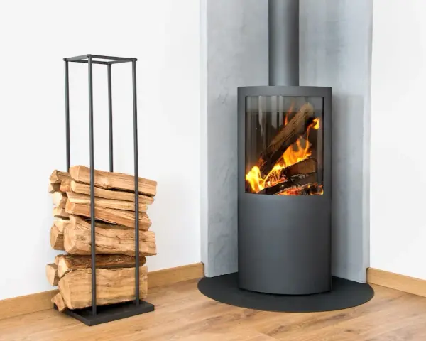 Un poêle à bois moderne, avec du bois empilé à côté, prêt pour le feu. Le placo mural met en valeur la distance parfaite pour la sécurité.