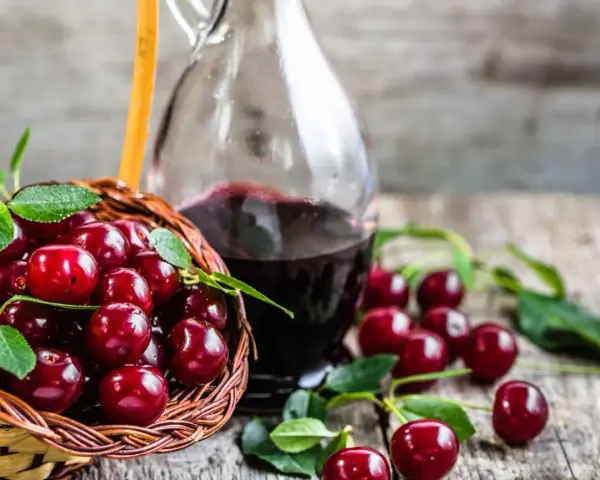 Koszyk pełen wiśni i butelka nalewki z wiśni – przepis babci. Aromatyczny trunek gotowy do degustacji.