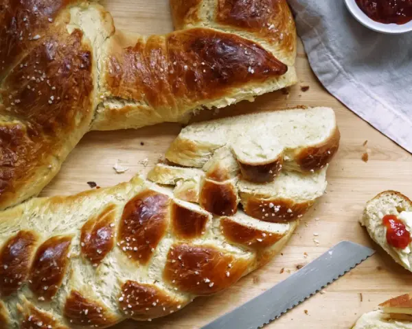 Goldbraune Neujahrsbrezel, mit Salz bestreut, auf einem Holztisch. Ein Stück ist mit Butter und Marmelade belegt. Ein tolles Neujahrsbrezel Rezept!
