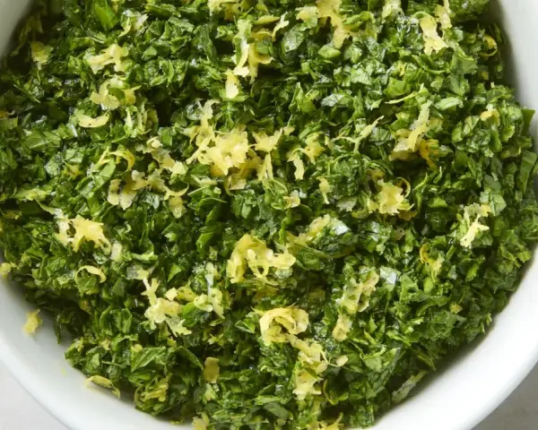 Un cuenco blanco lleno de perejil picado y ralladura de limón, perfecto para un toque fresco en tu cocina, como la albahaca en francés.