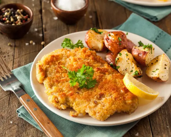 Perfekt paniertes Schnitzel mit Rosmarinkartoffeln und Zitrone. Ein Genuss, der zeigt, wie einfach und lecker Schnitzel panieren sein kann.