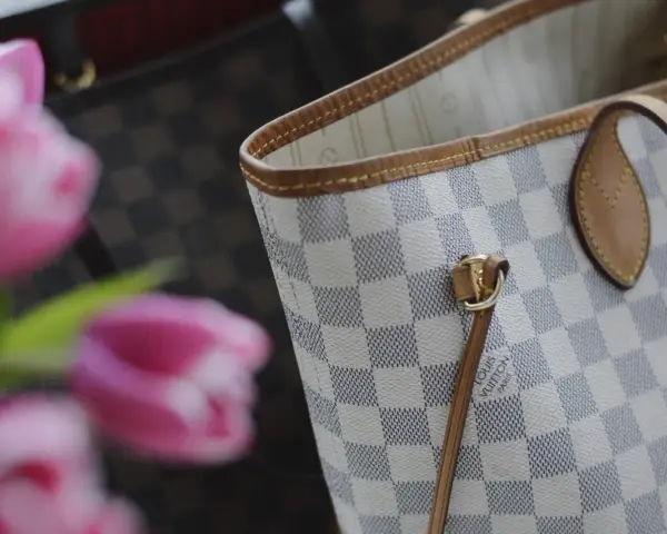 Jasna torebka Louis Vuitton w kratkę Damier Azur z różowymi tulipanami w tle.