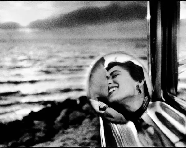 Un doux reflet dans le rétroviseur d'une voiture, une femme rit aux éclats, le regard tourné vers la mer.