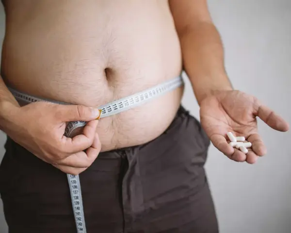 En person mäter sin midja med ett måttband, håller piller i handen. Kan indikera hormonell obalans och viktuppgång.