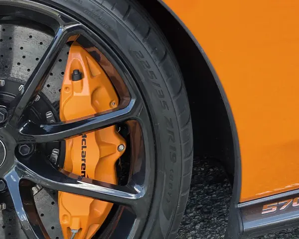 Pomarańczowy zacisk hamulcowy McLaren na czarnym, wieloramiennym kole. Opona z napisem 225/35 ZR19.