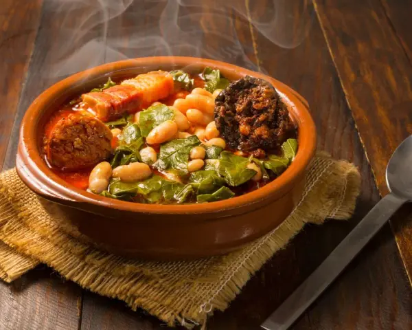 Un humeante pote asturiano, con fabes, berzas, chorizo y tocino, servido en cazuela de barro sobre arpillera.