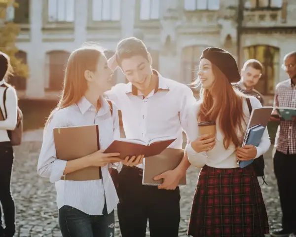 Studenci rozmawiający na kampusie, z książkami i notatkami w rękach. Wszyscy wyglądają na szczęśliwych, jakby właśnie skończyli zajęcia. To idealny obrazek dla osób, które chcą połączyć pracę z nauką, wybierając l4 a studia zaoczne.
