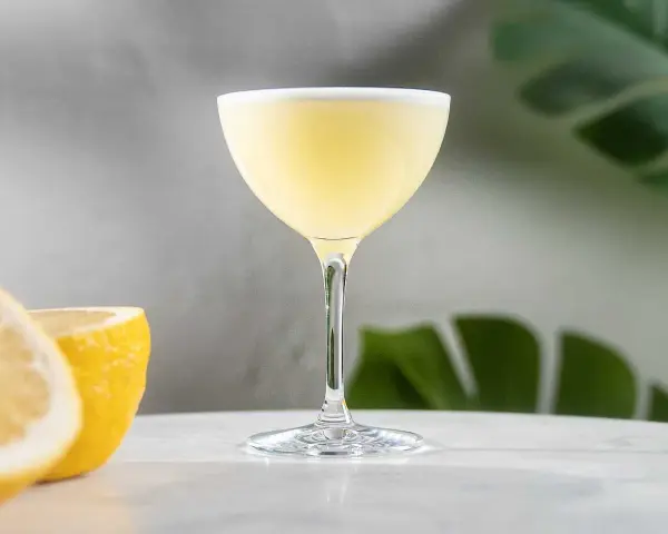 En elegant lemon martini med en lätt skumkrona, serverad med färska citronklyftor i bakgrunden.