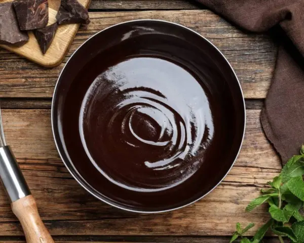 Lśniąca polewa kakaowa w misce, obok kawałki czekolady, trzepaczka i listki mięty.