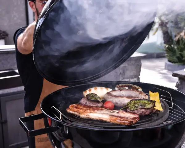 Fumo sale da una grigliata di carne succulenta, con salsicce, hamburger e pancetta che sfrigolano.