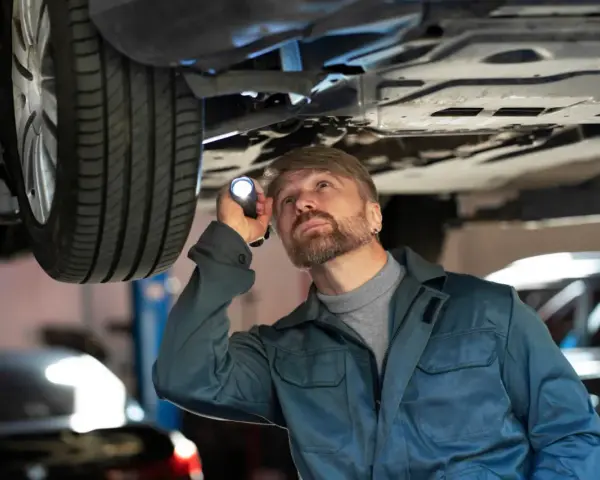 Mechanik z latarką bada podwozie auta, szukając problemów z jarzmem hamulca.