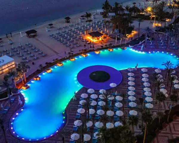 Luksusowy basen z niebieskim podświetleniem i leżakami na plaży w Dubaju.