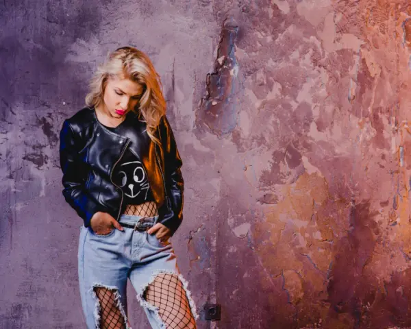 Blondynka w skórzanej kurtce i podartych dżinsach, z siatką na nogach, emanuje **grunge**'owym klimatem.