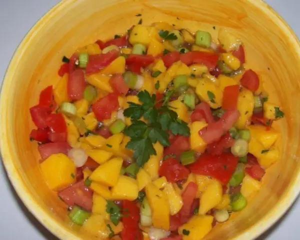 Bunte Mango Salsa mit Tomaten, Frühlingszwiebeln und Petersilie in einer gelben Schüssel.