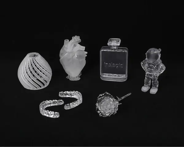 A collection of 3D printed acrylic objects: a vase, heart, dental aligners, perfume bottle, rose, and astronaut.