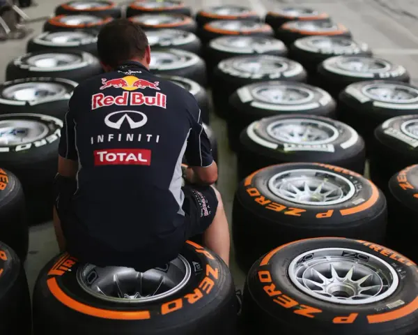 Mechanik w stroju Red Bulla siedzi wśród rzędów opon F1.