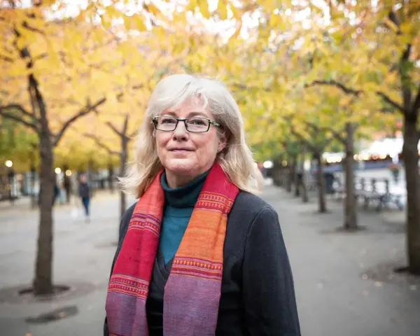 Kvinna med glasögon och färgglad scarf i höstpark. Hon verkar inte ha ont i leder brist på energi, utan njuter av den vackra naturen.