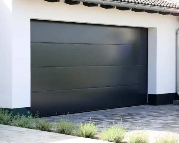 En modern, mörkgrå garageport montering med horisontella linjer. En vit fasad och grå stenläggning framför.
