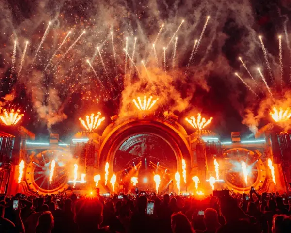 Spektakularny pokaz fajerwerków i płomieni na scenie podczas festiwalu Sunrise Festival 2026. Tłum ludzi z telefonami wzniesionymi ku górze.