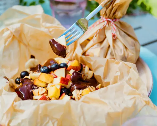 Fruchtiger Nachtisch vom Grill: Apfelstücke, Blaubeeren und Bananen mit Schokoladensauce, serviert in Papier.