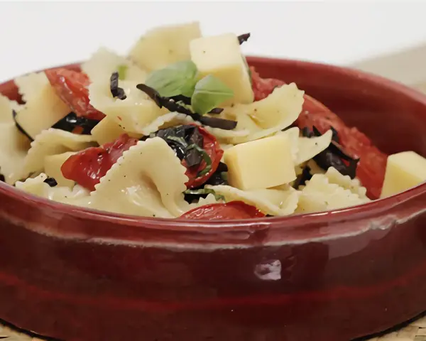 Deliciosa pasta farfalle con tomates secos, aceitunas negras, albahaca y cubos de queso. Una de las mejores recetas de pasta para disfrutar.