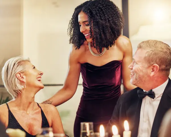 Drei Personen in eleganter Galadinner Kleidung lachen und unterhalten sich bei Kerzenlicht.