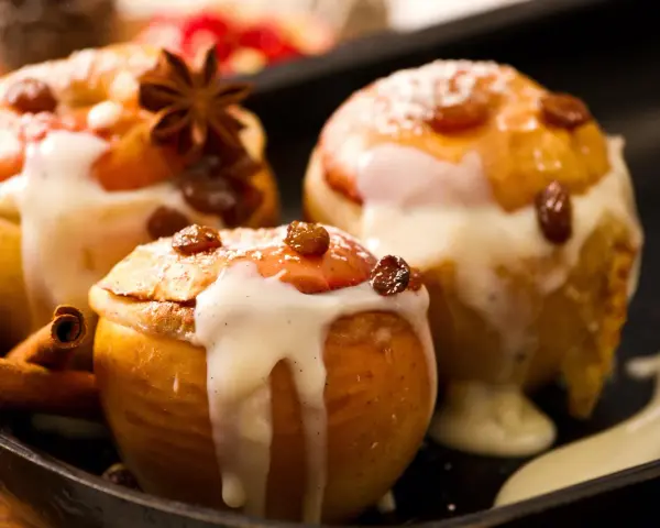 Drei köstliche Bratäpfel, übergossen mit Vanillesauce und garniert mit Rosinen und Zimtstangen. Ein perfektes Bratapfel Rezept für kalte Tage.