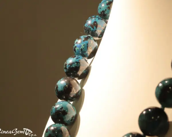 Collana di sfere in crisocolla pietra, con sfumature blu e nere, su sfondo chiaro e scuro.