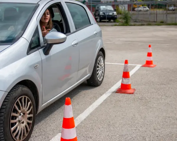 Młoda kobieta za kierownicą srebrnego samochodu ćwiczy jazdę na placu manewrowym. To może być jej droga do zdobycia prawa jazdy 17 lat.