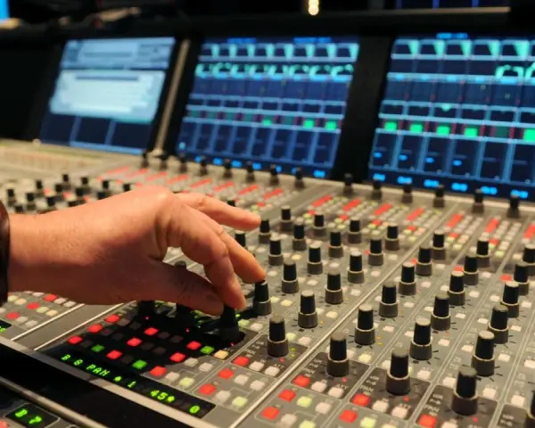 Hand am Mischpult, das an die Erfindung von Autotune erinnert. Tontechniker regelt Regler.
