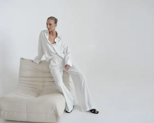 Elegancka kobieta w pasiastym komplecie, uosobienie quiet luxury, siedzi na kremowej sofie.