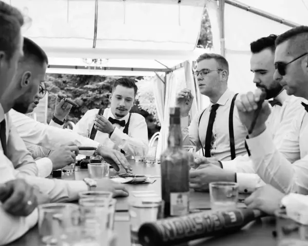 Panowie w eleganckich koszulach i szelkach świętują, paląc cygara i pijąc. Świetne kawalerski pomysły na wspólne chwile.