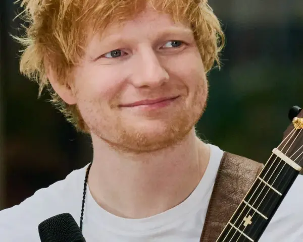 Ed Sheeran z gitarą, uśmiechnięty, w białej koszulce.