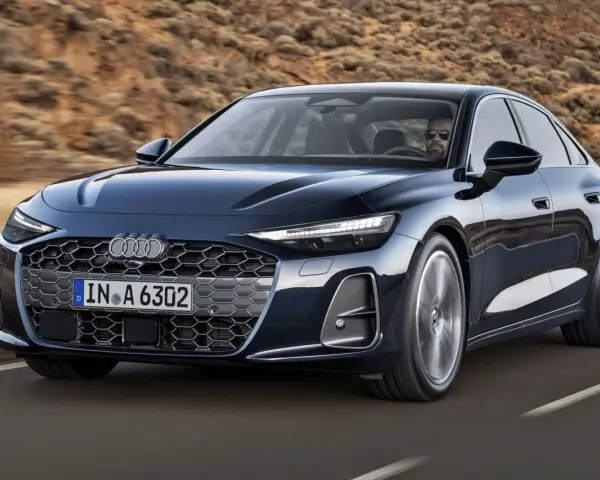 Elegancki, ciemnogranatowy Audi A6 sunie po drodze, z kierowcą w okularach za kierownicą.