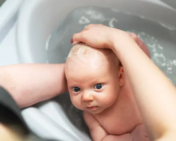 Niemowlę w wanience, myte przez rodzica. Czy można kąpać dziecko jak ma gorączkę? Woda może pomóc obniżyć temperaturę.