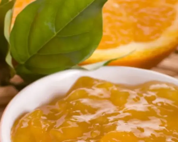 Una ciotola di marmellata di arance, con fette di arancia e foglie verdi sullo sfondo. Un'idea per un delizioso pesto al limone.