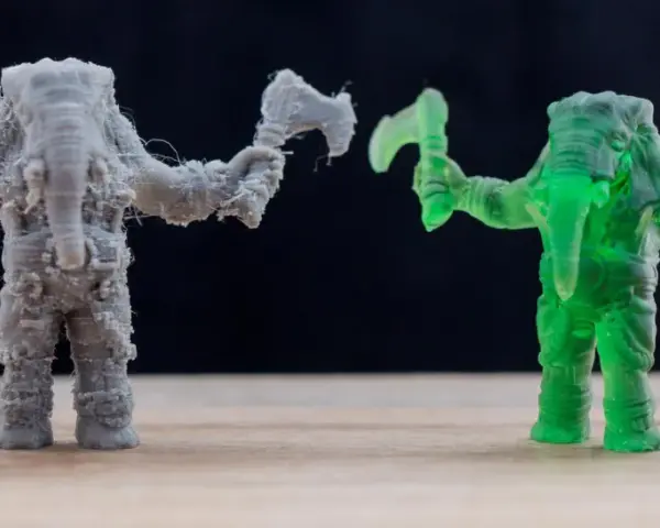 A grey FDM printed elephant warrior with stringing, and a translucent green resin printed elephant warrior, showcasing the difference between FDM vs resin printing.
