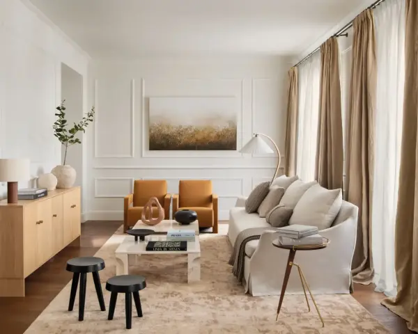 Elegante salón con salones con molduras en paredes, sofá blanco, sillones ocre y mesa de centro de mármol.