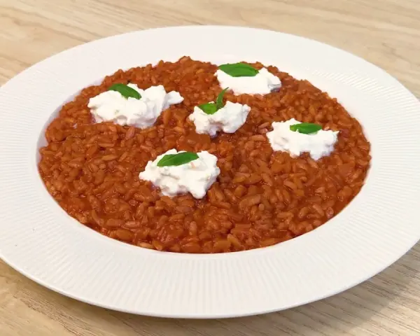 Un invitante risotto al pomodoro, arricchito da ciuffi di ricotta fresca e basilico, pronto per essere gustato.