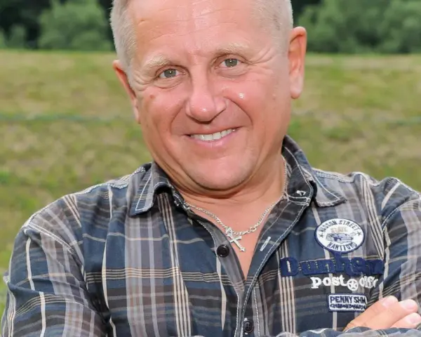 Uśmiechnięty mężczyzna w kratę, z krzyżykiem na szyi. To Bercik, znany z serialu.